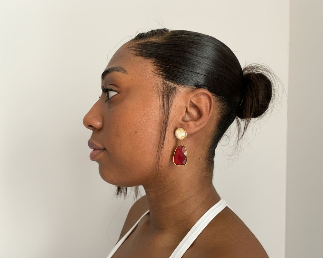 Close-up of a girl wearing a red and gold earring against a neutral background