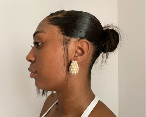 Woman wearing pearl tear gold 18k gold earrings with a neutral background
