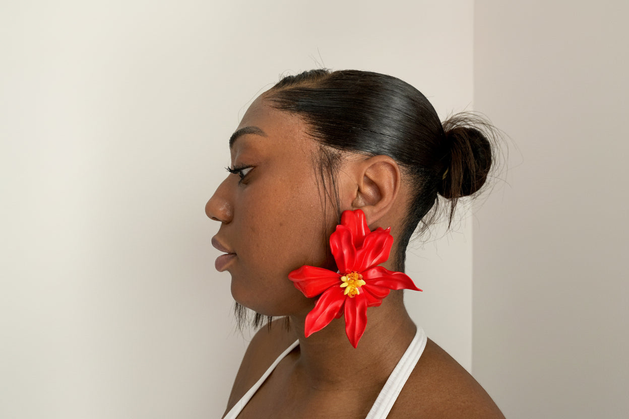 Woman wearing a large red flower earring against a plain background