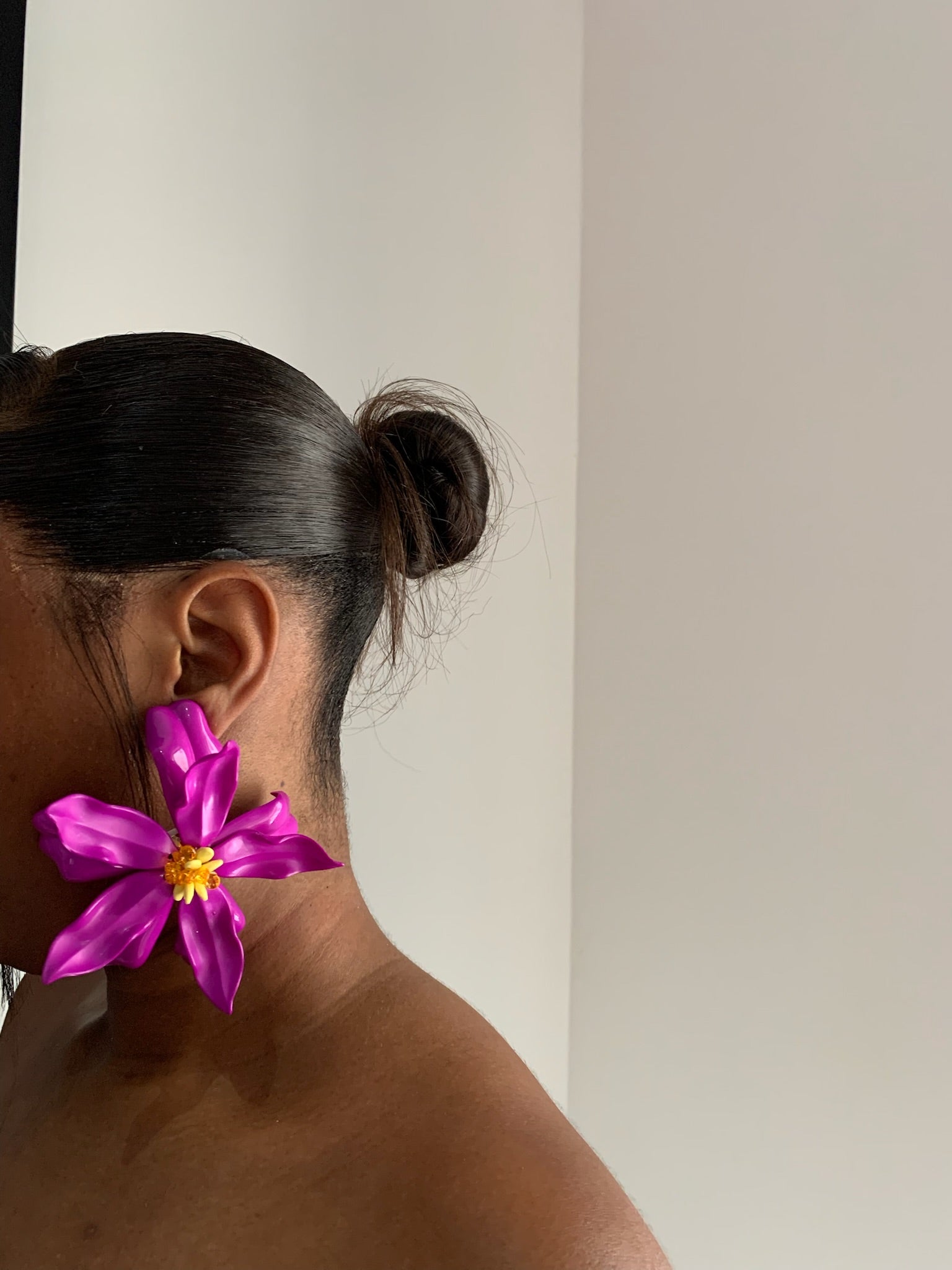 Person wearing a  big bright purple flower earring against a neutral background