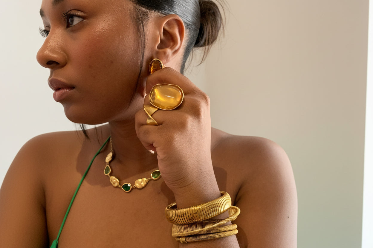 Model wearing gold jewelry including earrings, ring, and bracelets.