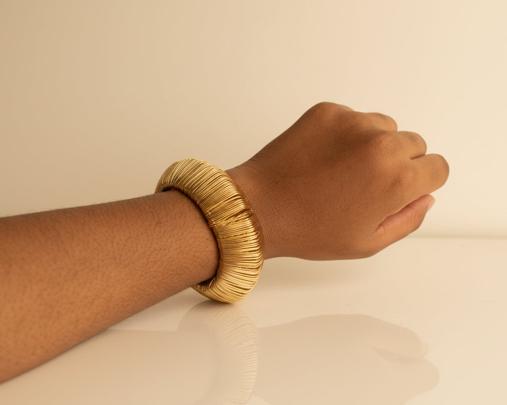 Hand wearing a gold bracelet against a plain background