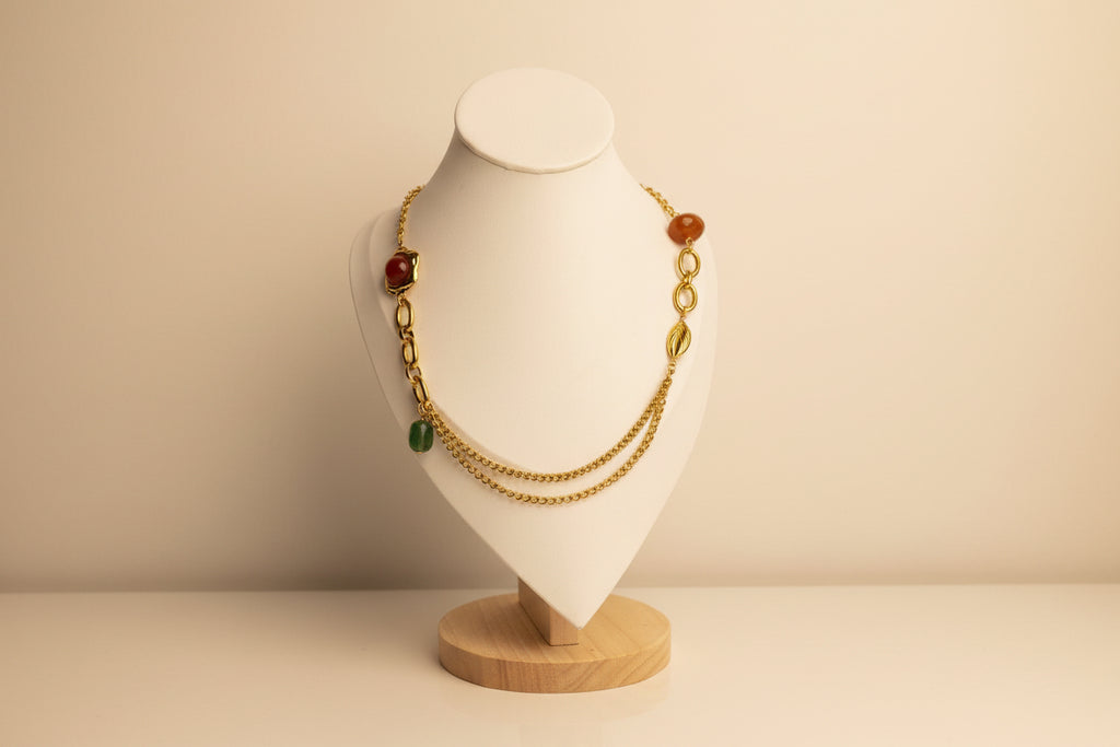 Gold necklace with red and green beads on a white mannequin bust.