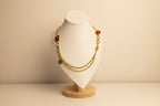 Gold necklace with red and green beads on a white mannequin bust.
