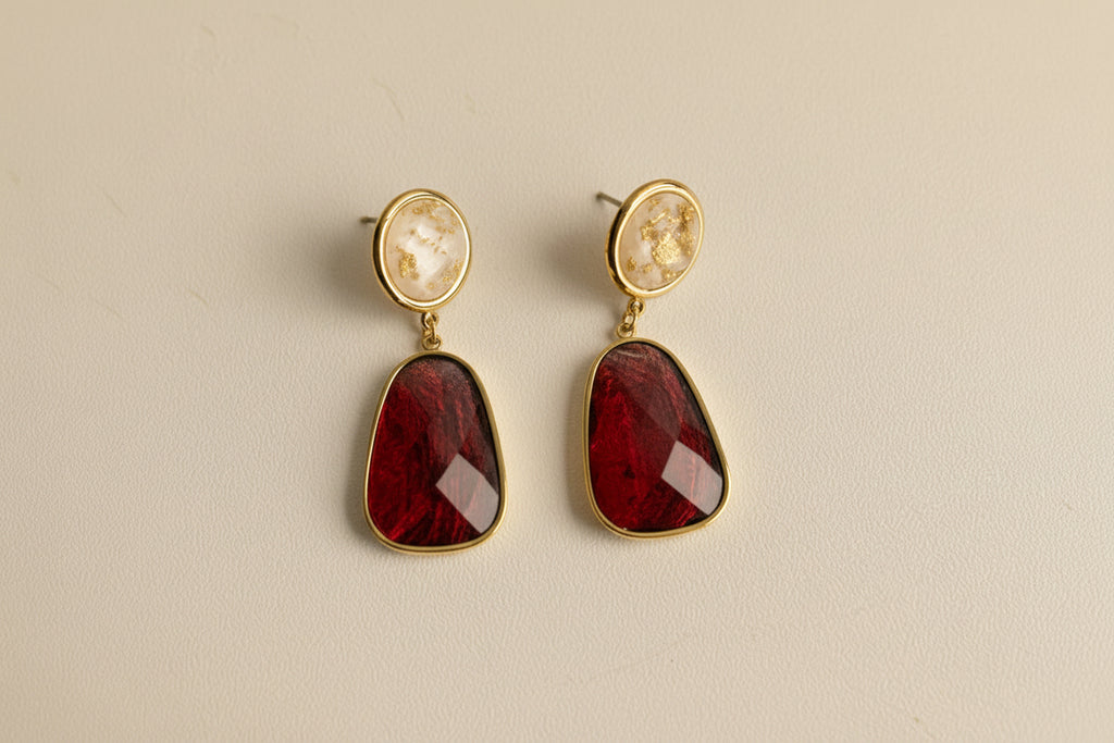Pair of earrings with red stones and gold accents on a light gray background