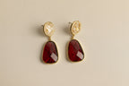 Pair of earrings with red stones and gold accents on a light gray background