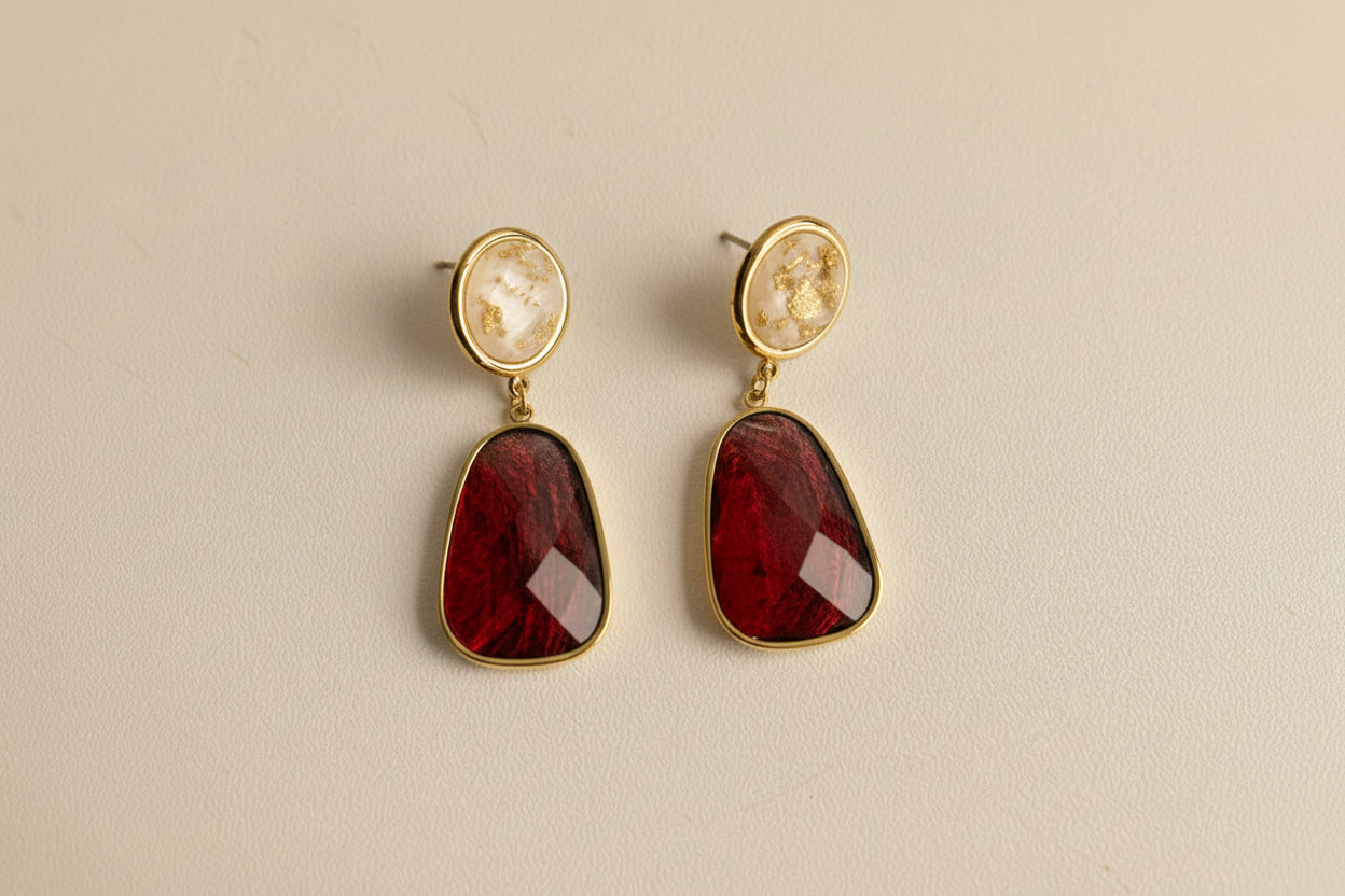 Pair of earrings with red stones and gold accents on a light gray background